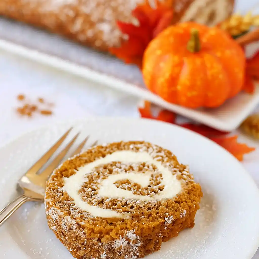 Slice of pumpkin roll cake with cream cheese frosting swirl